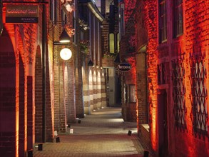 Romantic illuminated narrow alley with red lights and old buildings at night, Bremen, germany