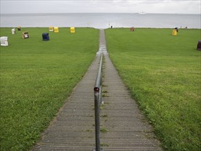 A path leads to the coast with colourful beach chairs on a green meadow, cuxhaven, germany