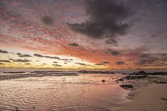 Sunrise over the sea with gentle waves. Sandy beach with lava rocks and blue water alternating with