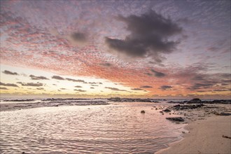 Sunrise over the sea with gentle waves. Sandy beach with lava rocks and blue water alternating with