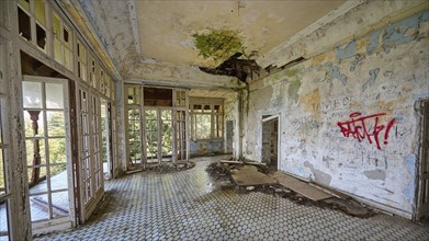 Abandoned room with broken roof, graffiti on the walls and light coming in through the windows,