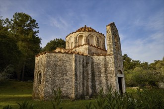 A small church with stone walls and red bricks, surrounded by trees under a blue sky, Byzantine