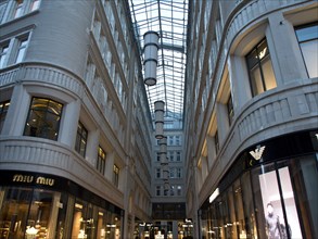 Modern shopping arcade with a glass roof, flanked by shop windows and well-lit shops, Vienna,