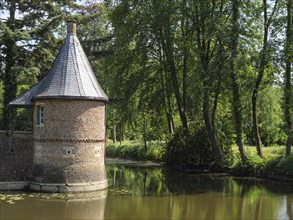 Round tower on a moat with a reflecting water surface, surrounded by summer trees and a peaceful