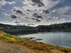 A natural dam on a lake with boats and dramatic clouds in the sky in a hilly landscape, Waldeck,