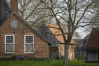 Old brick farmhouse with wooden doors and windows, surrounded by trees and a rural setting, Vreden,