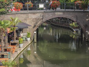 A bridge over a canal with water and flower arrangements. Summer atmosphere with shadows and