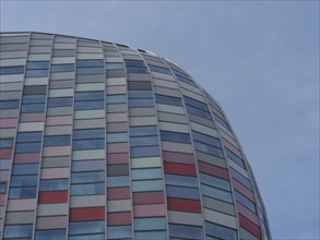 Modern glass façade of a curved building with colourful windows and a cloudless sky, utrecht,