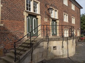 Old brick house with green doors, windows and a side staircase with wrought-iron railings,