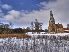 Winter castle surrounded by snowy landscape and reeds, under a cloudy sky, Raesfeld, münsterland,