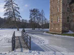 Historic castle and frozen river in winter with snow-covered terrain and bridge, sunny and clear,