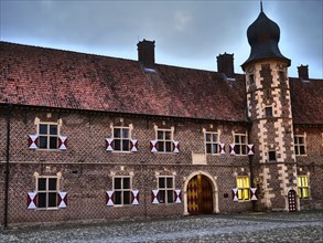 Historic castle with corner tower at dusk, brick façade with many windows and decorative doors,