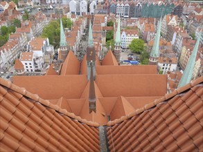 View from a red tiled roof of the city and several church towers rising from the roofs of the old
