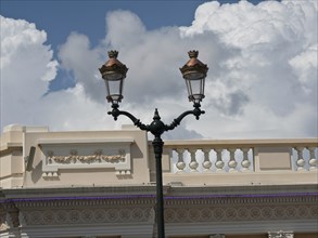 Historic street lamp in front of an old building with a sky full of clouds in the background,