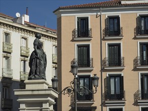 Statue in front of a historic building with windows, balconies and a lantern against a blue sky,