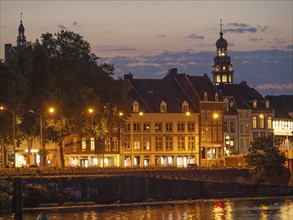 City view at dusk with historic buildings and illuminated tower and river reflections, Maastricht,