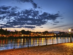 Evening river promenade with city lights and calm atmosphere under a cloudy sky, Maastricht,