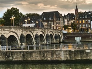 Historic bridge over a river, surrounded by an illuminated city at dusk, Maastricht, limburg,