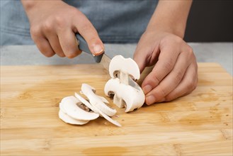 Cutting champignon mushrooms on a wooden board, prepare salad, healthy food with vegetables, fresh