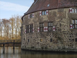 Part of a moated castle with red and white shutters, adjacent to a bridge and water, lüdinghausen,