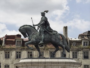 A statuesque equestrian figure in armour on a horse under a slightly cloudy sky in front of old
