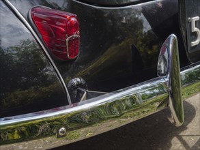 Close-up of a black vintage car, focussed on the rear light and the chrome bumper, winterswijk,