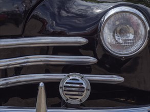 Close-up of a black classic car, showing the front headlight and the chrome grille, winterswijk,