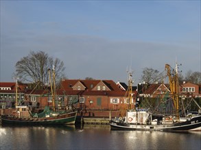 Fishing boats lying in the calm waters of a harbour with red houses in the background, greetsiel,