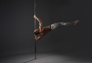 Image of strong gymnast exercising on pylon in studio