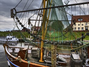 A rustic fishing boat with a net in the harbour. Water, jetties and a cloudy sky, Greetsiel, East