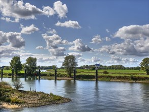 River landscape with green meadows and trees in the background, under a sky full of white clouds,