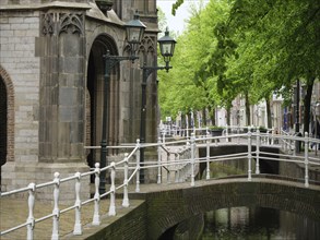 Historic buildings and lanterns along a bridge over a canal with green trees, Delft, Holland,