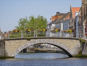 Stone bridge over a canal, decorated with flower boxes and historical buildings in the background,