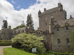 Castle with high towers and stone walls under a cloudy sky, surrounded by green lawns, inverness,