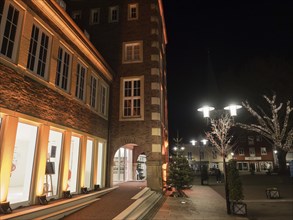 An illuminated modern building at night with large windows, street lamps and trees in the