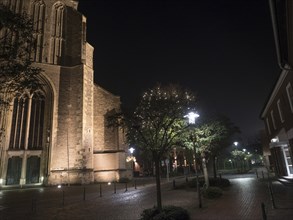 Illuminated church in a quiet night atmosphere with trees on a cobbled pavement, bocholt,