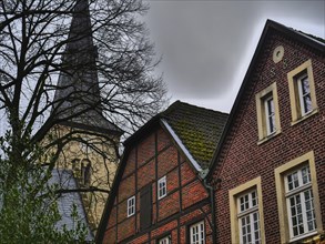 Roofs of half-timbered houses in front of a church with a dark church tower on a cloudy day,
