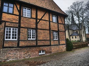 Half-timbered brick house with white windows in an autumnal ambience, church in the background,