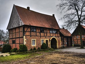 A half-timbered house with red bricks, surrounded by bare trees on a cloudy day, asbeck, legden,