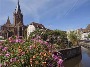 Historic town with flowers by the river, in the background a church and old buildings under a blue