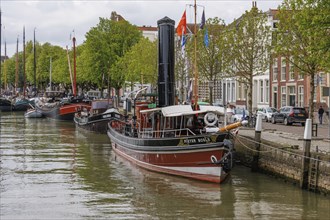A steamboat in the harbour, surrounded by other boats and historic buildings, several flags can be