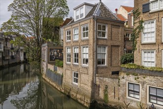Historic brick houses with murals along a quiet canal with reflection in the water, Dordrecht,