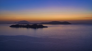 A calm sunset over the sea, the islands in the background surrounded by a gentle colour gradient of