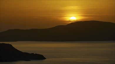 A peaceful seascape at sunset, hills in the background, illuminated by warm golden light, Makri