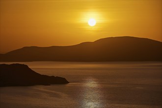 The sun sets over a calm sea and rolling hills, bathing the scene in warm orange, Makri Island,