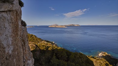 View from a cliff to the open sea and several islands in the distance under a blue sky, Makri