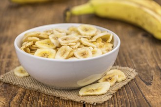 Homemade Dried Banana Chips on an wooden table as detailed close-up shot, selective focus