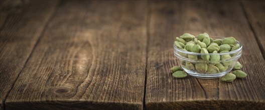 Wasabi coated Peanuts as high detailed close-up shot on a vintage wooden table (selective focus)