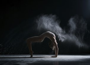 Modern art. Dancer performs acrobatic trick in cloud of dust