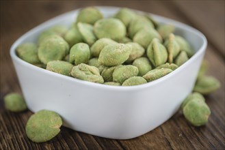 Wasabi coated Peanuts as high detailed close-up shot on a vintage wooden table (selective focus)